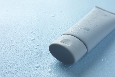 Moisturizing cream in tube on light blue background with water drops, closeup. Space for text
