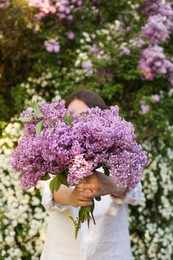 Photo of Woman holding lilac flowers in front of her face outdoors