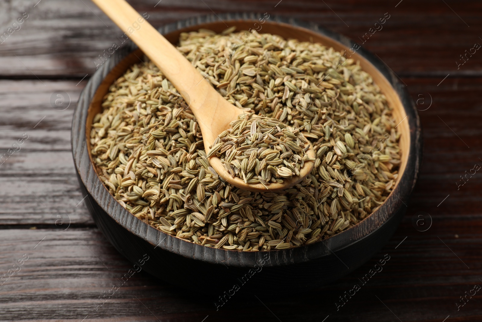 Photo of Spoon with fennel seeds in bowl on wooden table, closeup