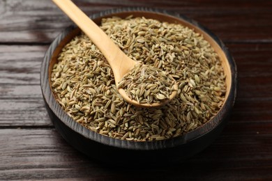 Spoon with fennel seeds in bowl on wooden table, closeup
