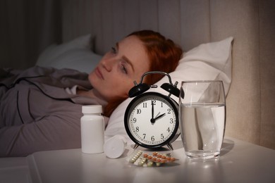 Woman suffering from insomnia in bed at home, focus on pills and alarm clock