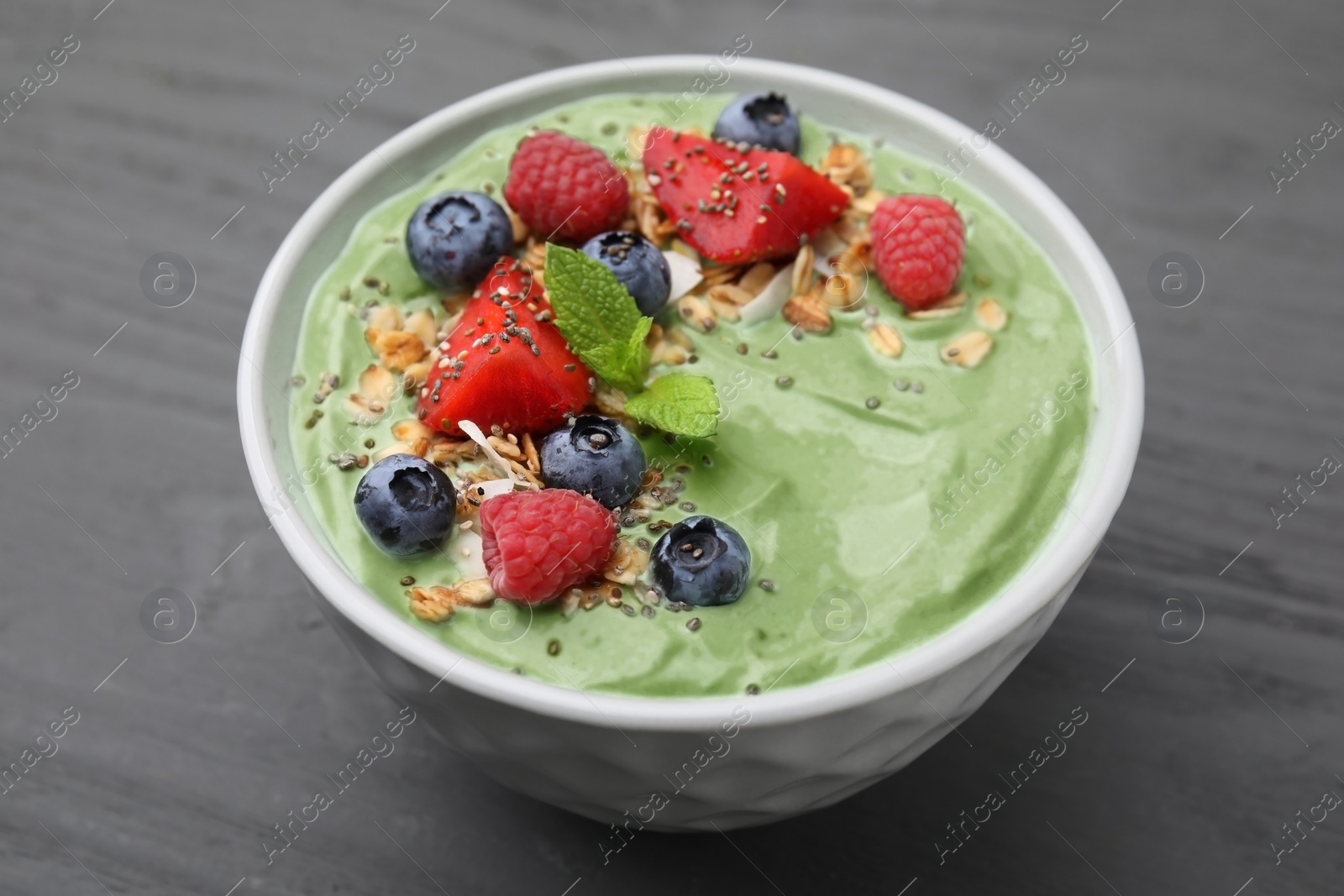 Photo of Tasty matcha smoothie bowl served with berries and oatmeal on grey wooden table, closeup. Healthy breakfast