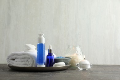 Photo of Spa composition. Cosmetic products, terry towel, burning candles and sea salt on gray table against light background, space for text