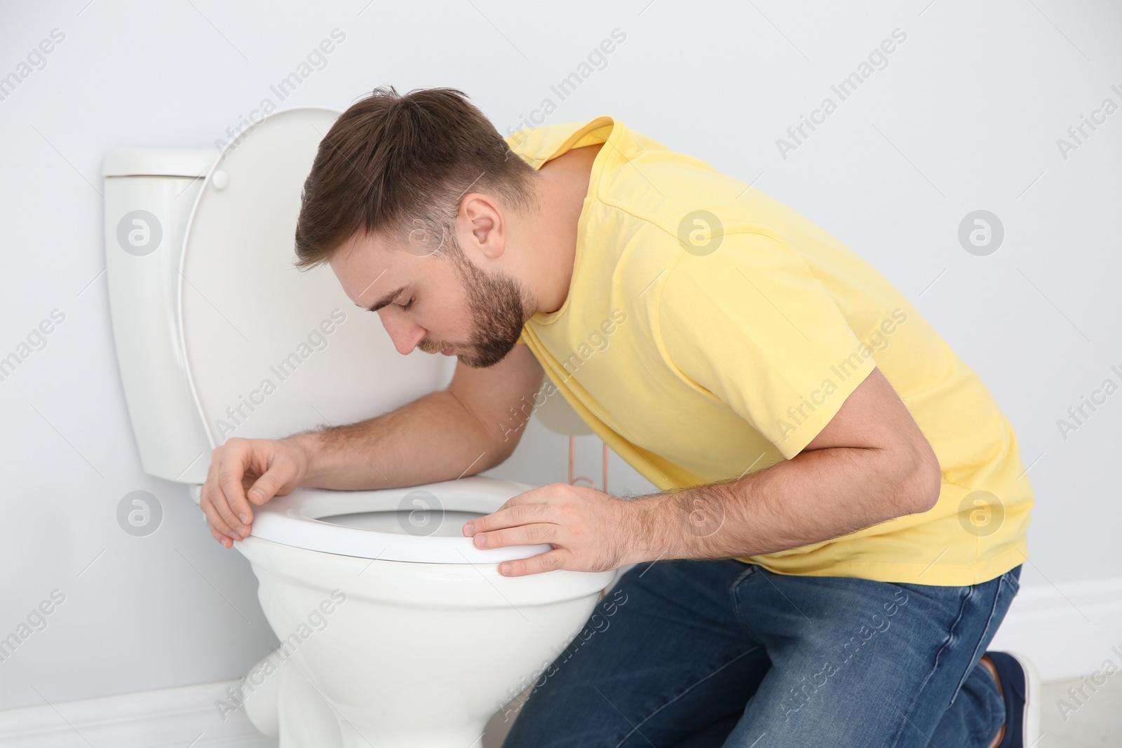 Photo of Young man suffering from nausea over toilet bowl indoors