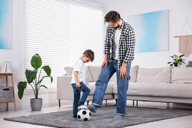 Photo of Happy dad and son playing football on carpet at home