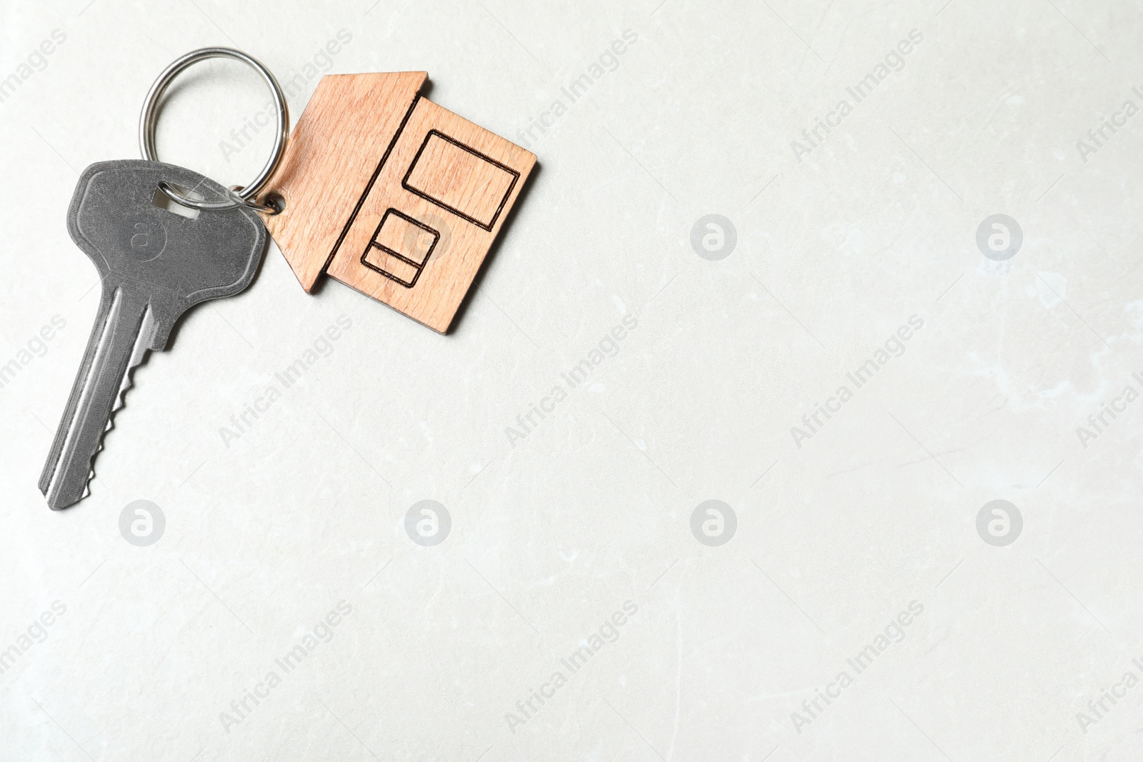 Photo of Key with trinket in shape of house on grey marble background, top view and space for text. Real estate agent services