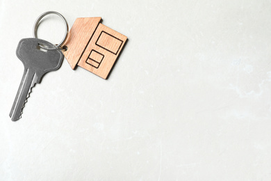 Key with trinket in shape of house on grey marble background, top view and space for text. Real estate agent services