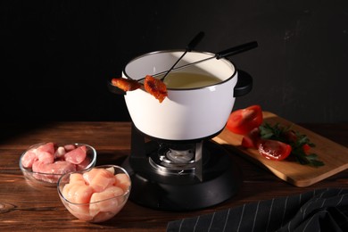 Fondue pot, forks with fried meat pieces and other products on wooden table