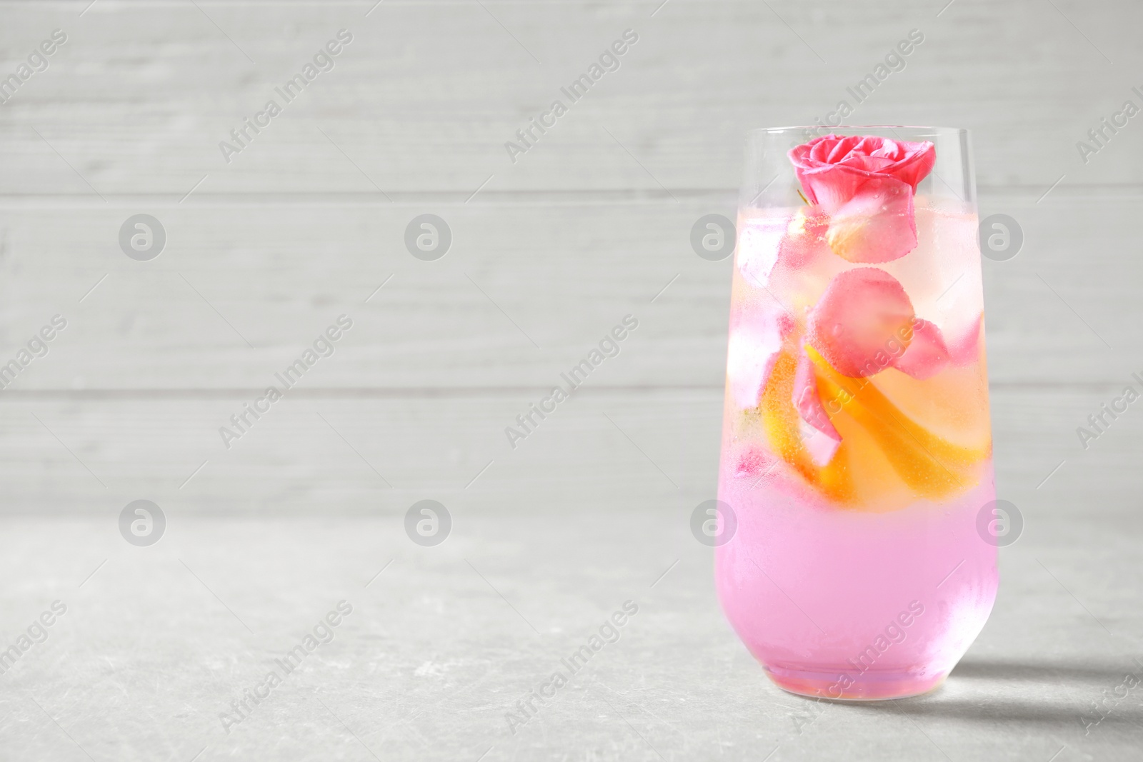 Photo of Glass of delicious refreshing drink with lemon and roses on table. Space for text