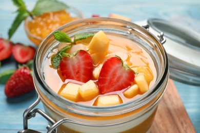 Photo of Delicious panna cotta with mango coulis and fresh fruit pieces on light blue table, closeup