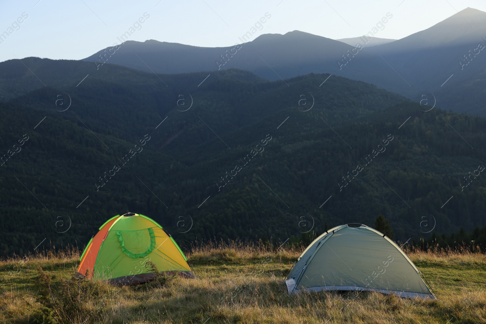 Photo of Two color camping tents on hill in mountains