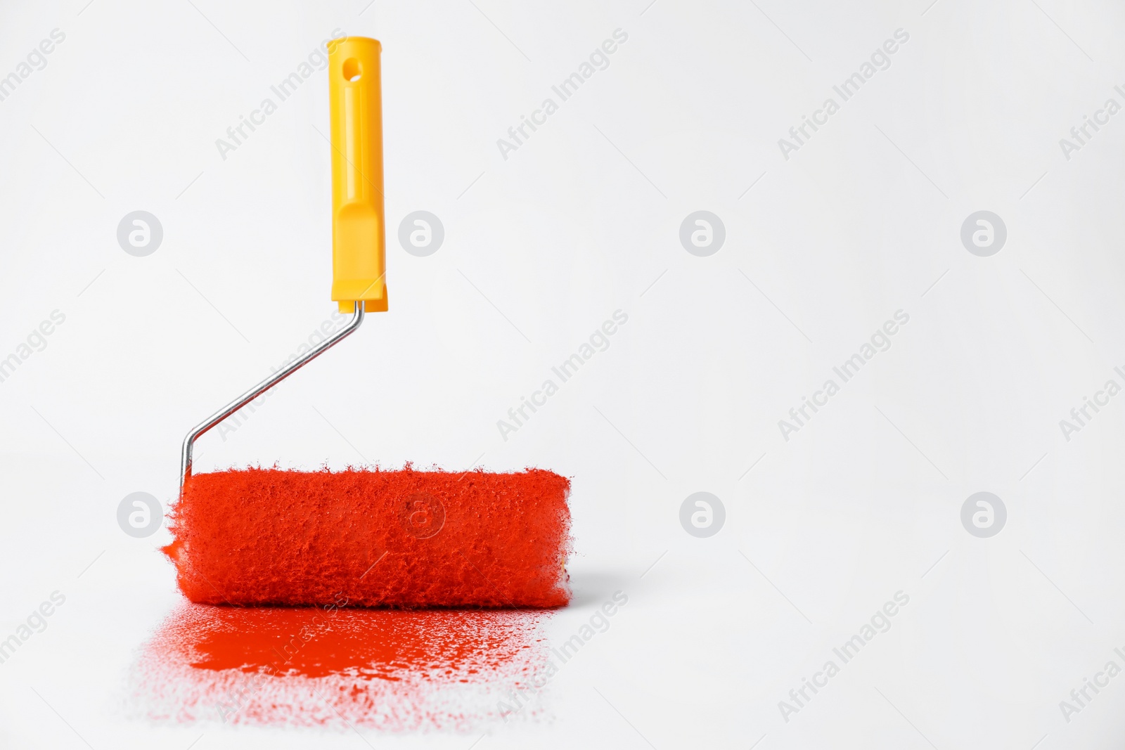 Photo of Roller brush and strokes of orange paint on white background. Space for text