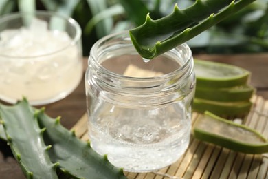 Photo of Dripping aloe vera gel from leaf into jar at table, closeup