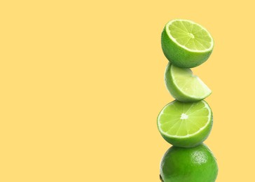 Stacked cut and whole limes on pale yellow background, space for text