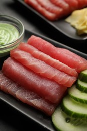 Photo of Tasty sashimi (pieces of fresh raw tuna) and cucumber slices on black plate, closeup
