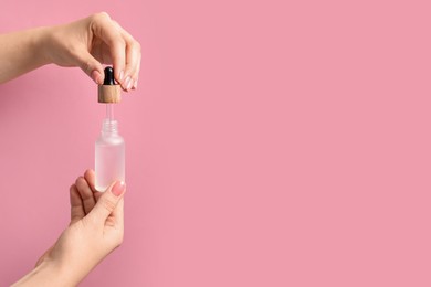 Photo of Woman dripping serum from pipette into bottle against pink background, closeup. Space for text