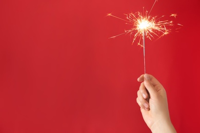 Photo of Woman holding bright burning sparkler on red background, closeup. Space for text