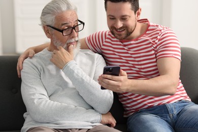 Photo of Happy son and his dad watching something on smartphone at home