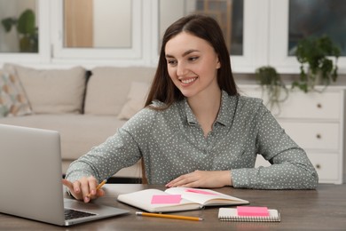 Woman with notebook working on laptop at wooden table indoors