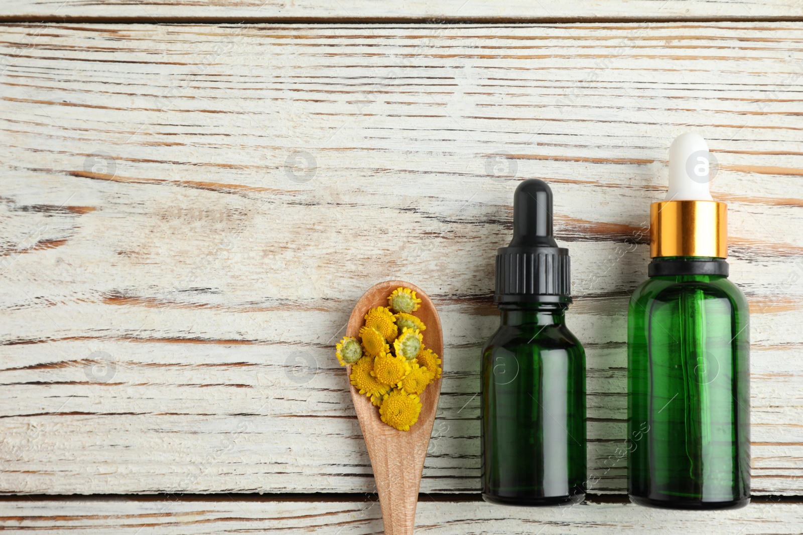 Photo of Bottles of essential oil and spoon with flowers on wooden table, flat lay. Space for text