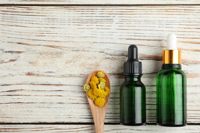 Photo of Bottles of essential oil and spoon with flowers on wooden table, flat lay. Space for text