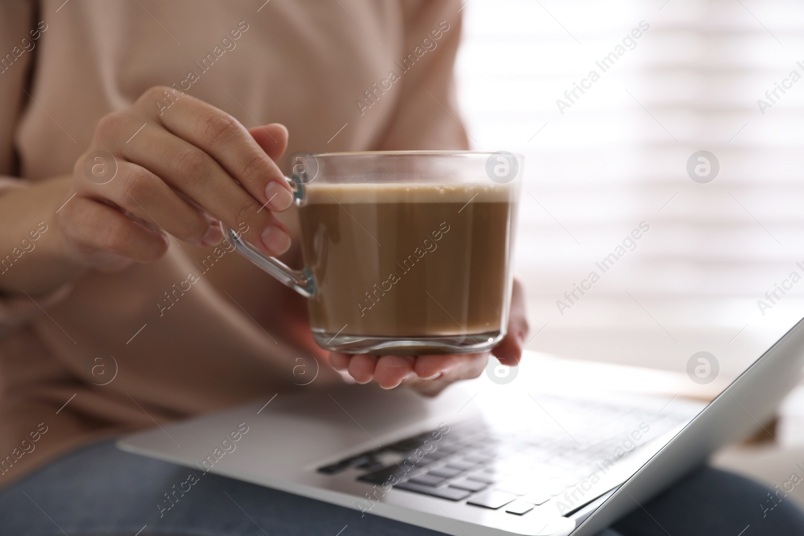 Photo of Woman with cup of coffee and laptop indoors, closeup