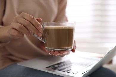 Photo of Woman with cup of coffee and laptop indoors, closeup