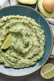 Photo of Delicious guacamole with lime and fresh avocado on table, flat lay