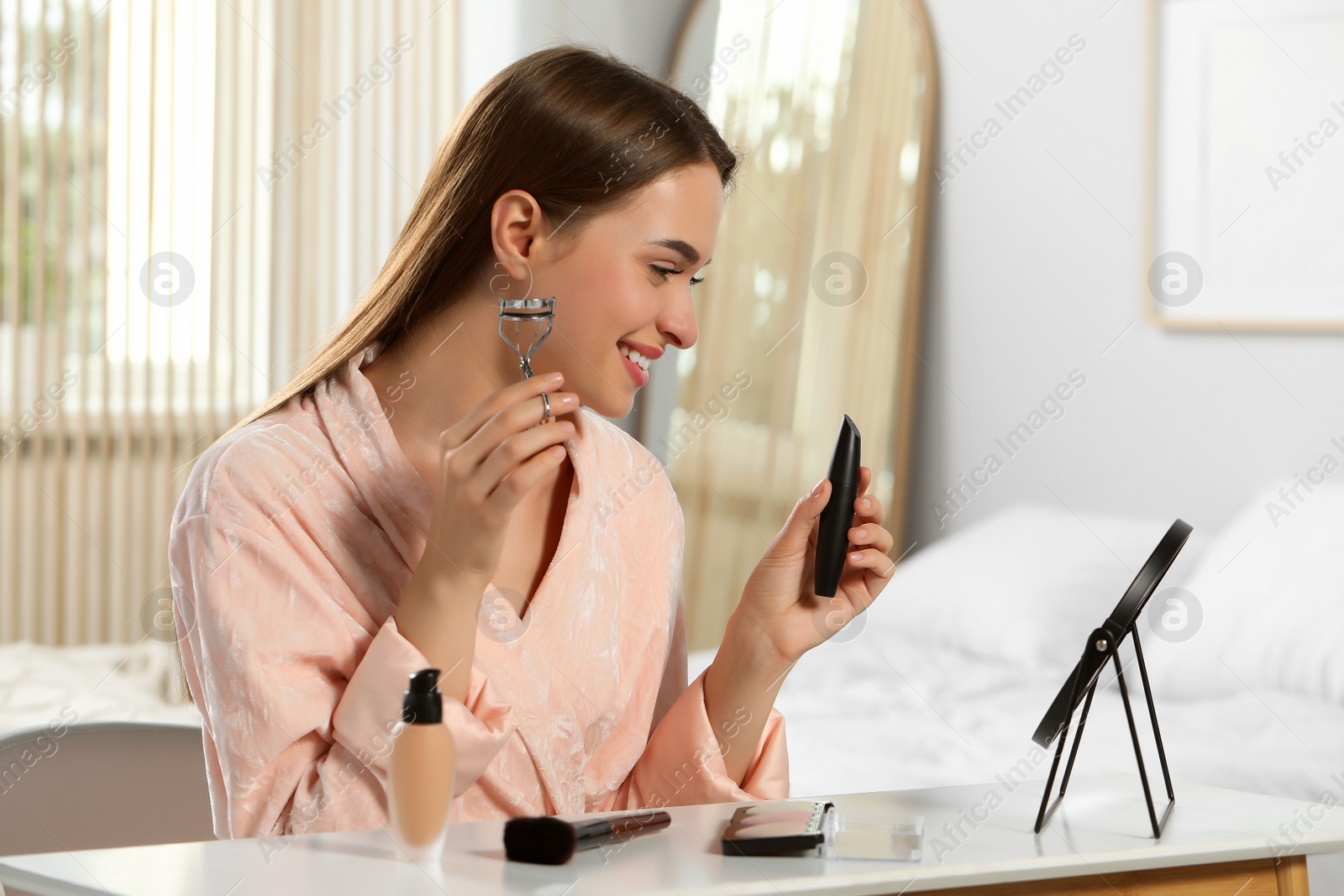 Photo of Woman with eyelash curler and lipstick near mirror at home