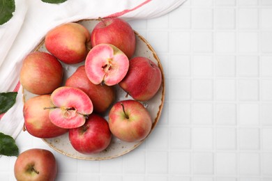 Photo of Tasty apples with red pulp and leaves on white tiled table, flat lay. Space for text