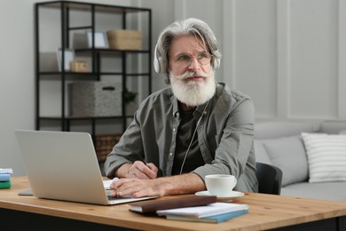 Photo of Middle aged man with laptop and headphones learning at table indoors