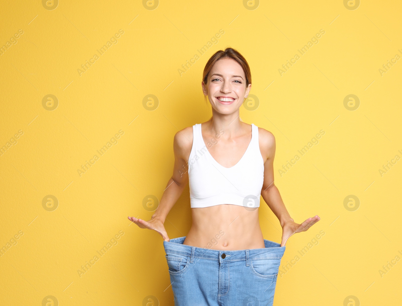 Photo of Young slim woman in old big jeans showing her diet results on color background