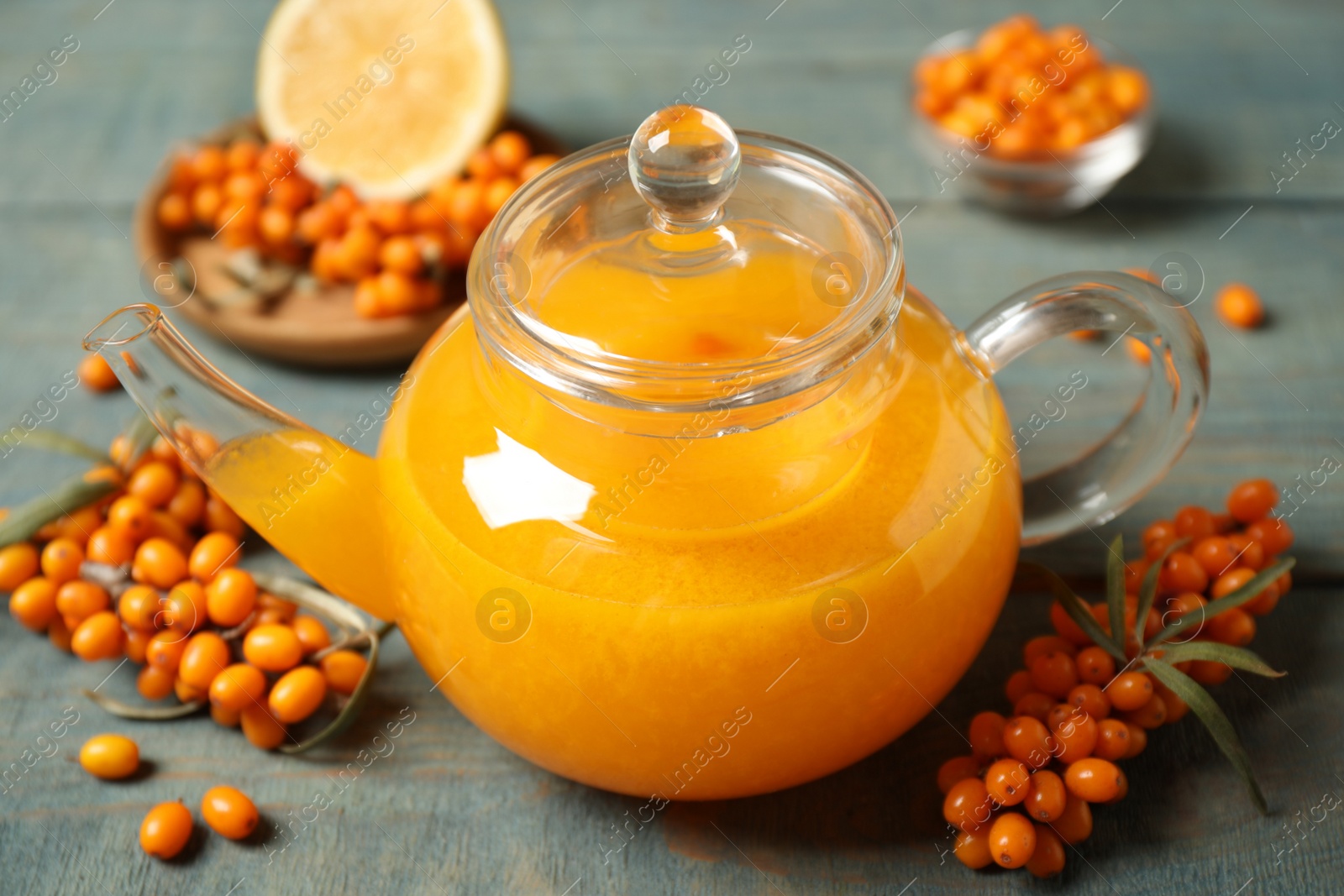 Photo of Delicious sea buckthorn tea and fresh berries on blue wooden table, closeup