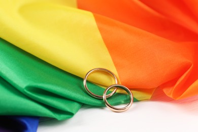Rainbow LGBT flag and wedding rings on white wooden table, closeup