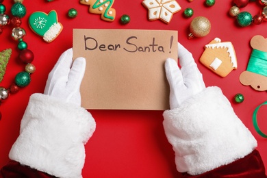 Photo of Santa Claus with letter and Christmas decor on red background, top view