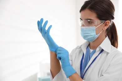 Photo of Doctor in protective mask and glasses putting on medical gloves against light background