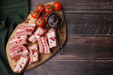 Photo of Cut raw pork ribs with peppercorns, tomatoes and sauce on wooden table, top view. Space for text
