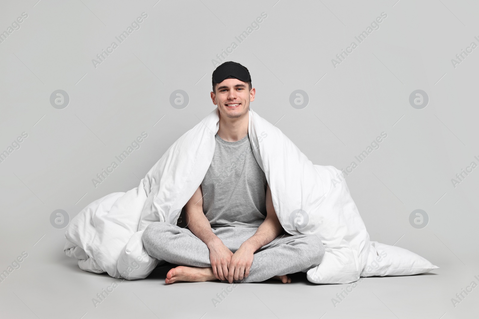 Photo of Happy man in pyjama and sleep mask wrapped in blanket on grey background