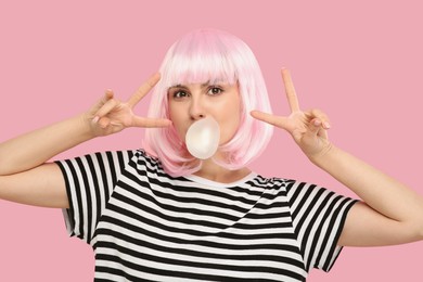 Photo of Beautiful woman blowing bubble gum and gesturing on pink background