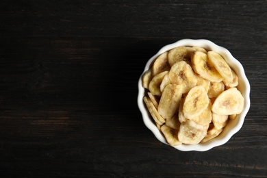 Photo of Bowl with sweet banana slices on wooden  table, top view with space for text. Dried fruit as healthy snack