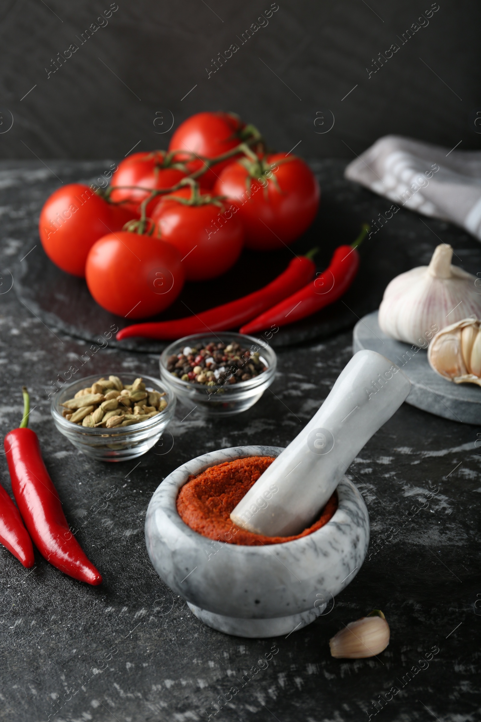 Photo of Mortar with red curry paste and ingredients on black textured table