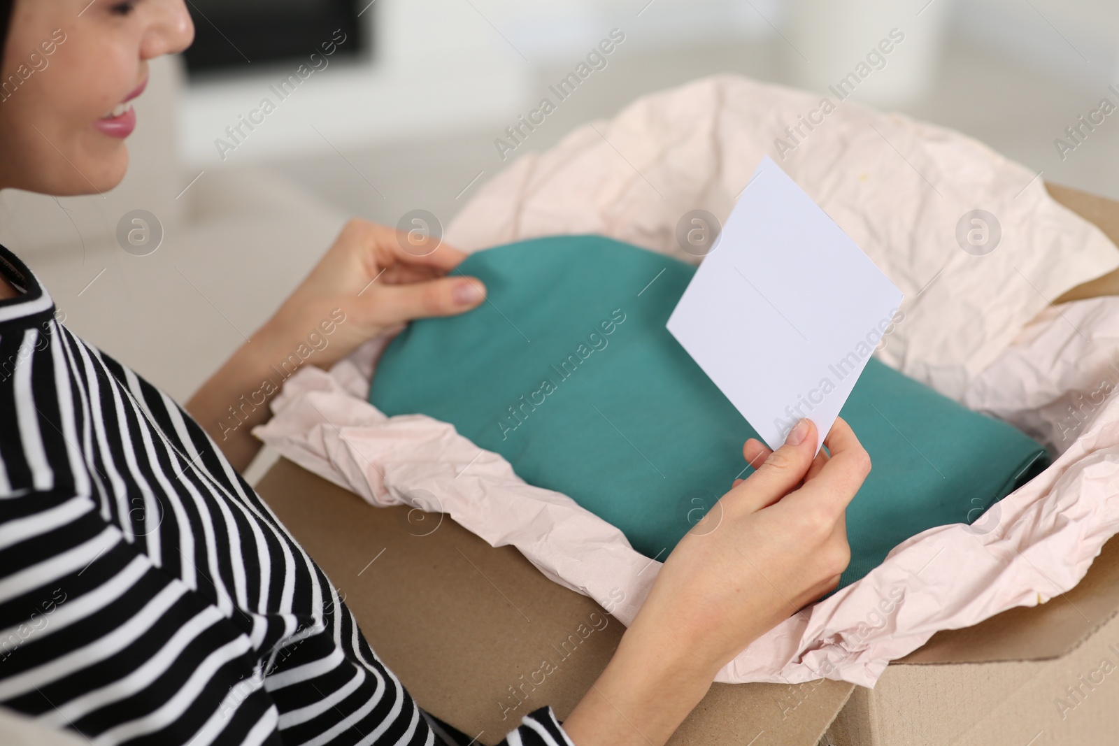 Photo of Happy woman holding greeting card near parcel with Christmas gift at home, closeup