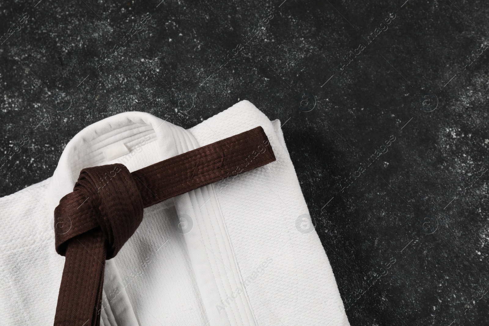 Photo of Brown karate belt and white kimono on gray textured background, top view. Space for text