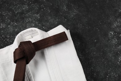 Brown karate belt and white kimono on gray textured background, top view. Space for text