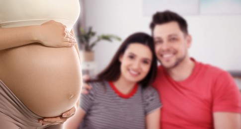 Image of Surrogacy concept. Young pregnant woman and blurred view of happy couple indoors, banner design