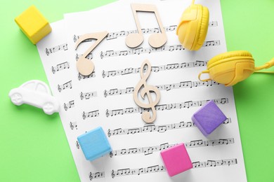 Wooden notes, music sheets, headphones and toys on light green background, flat lay. Baby song concept