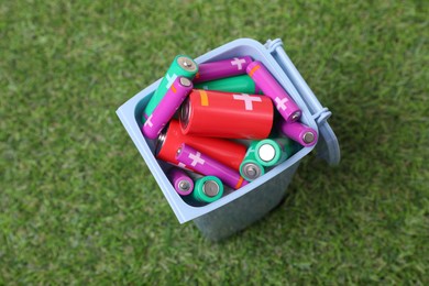 Photo of Many used batteries in recycling bin on green grass, above view
