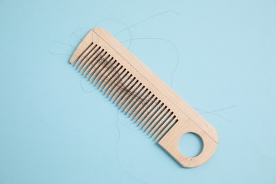 Photo of Wooden comb with lost hair on light blue background, top view
