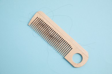 Wooden comb with lost hair on light blue background, top view