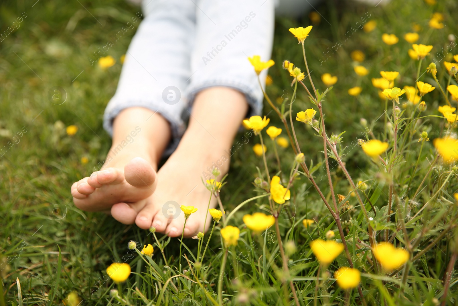 Photo of Woman sitting barefoot on green grass outdoors, closeup